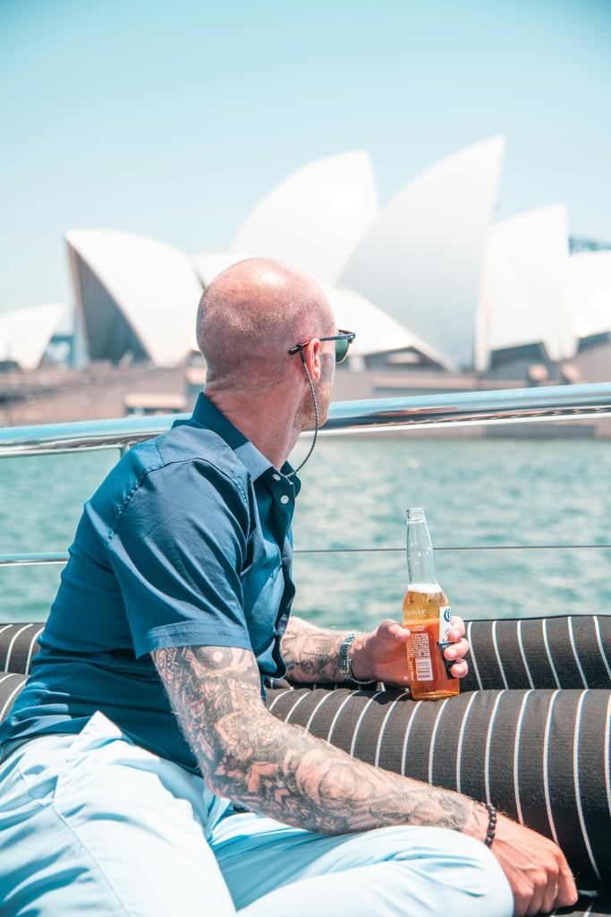 man sipping a beer on a boat in front of Sydney Opera House