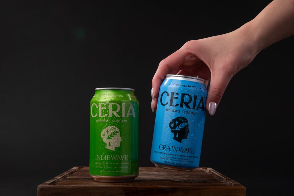 Two cans of alcohol-free beer on a wooden table, with a hand grabbing one of them